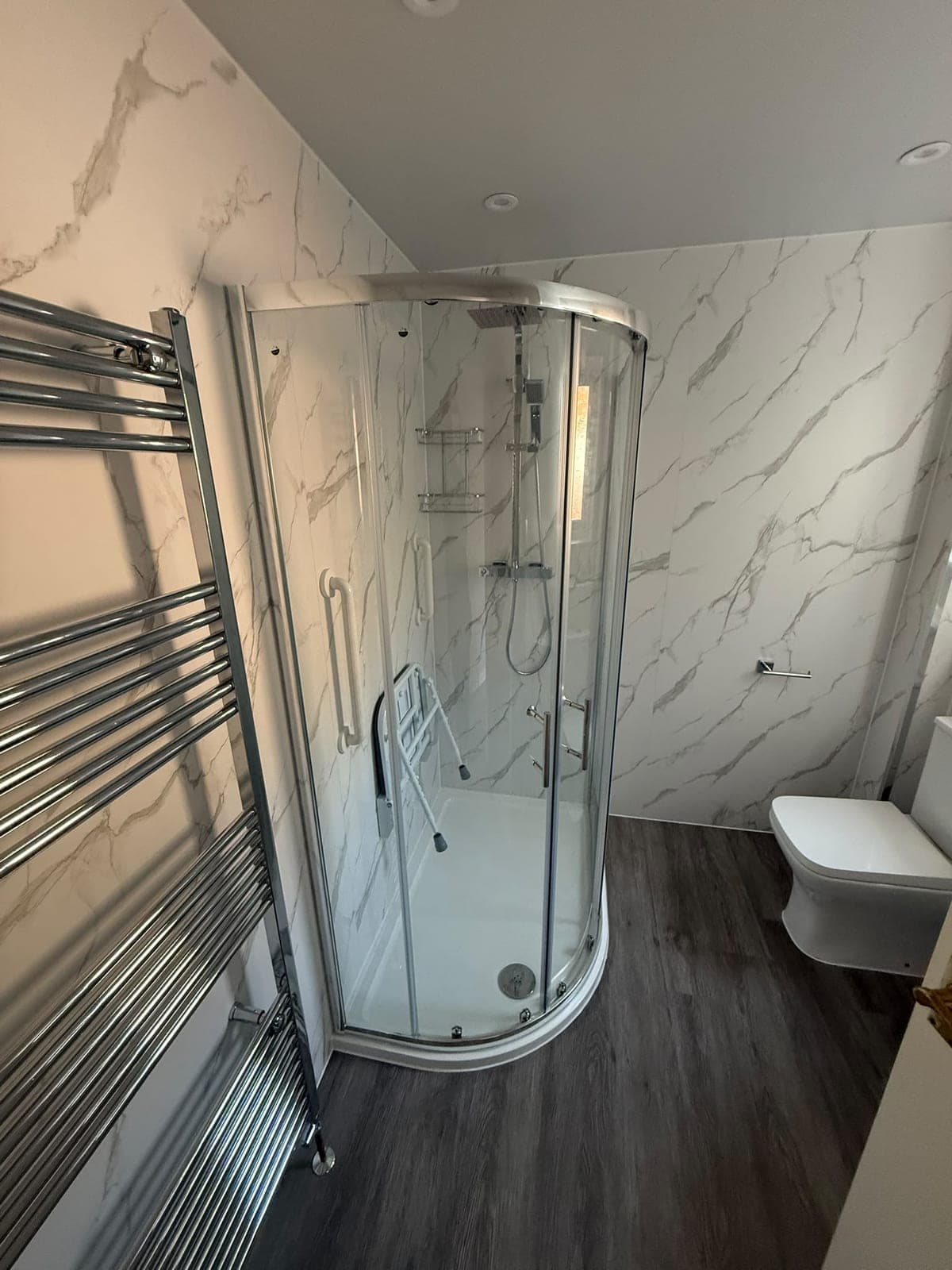 Easy-access shower room with a quadrant enclosure, fold-down seat, grab rails and marble-effect wall panels, Edinburgh